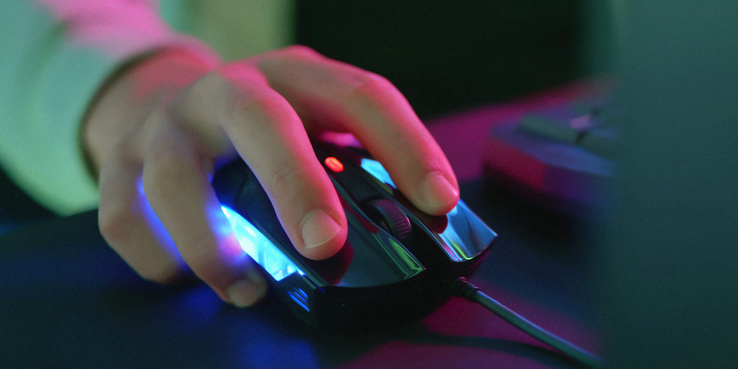 Brightly colored, close-up photograph of a hand on a gaming mouse