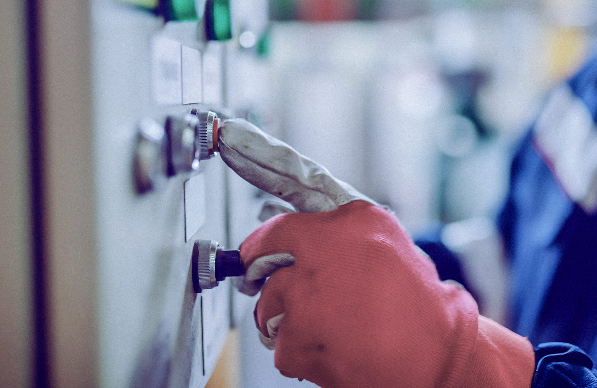 Close-up photo of an index finger pressing a button on a control panel in an industrial setting