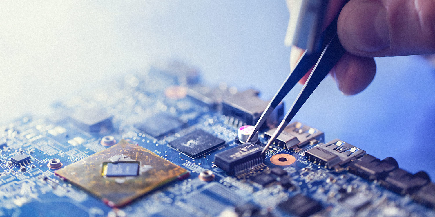 A computer chip, held by a pair of tweezers, is placed onto a PCB